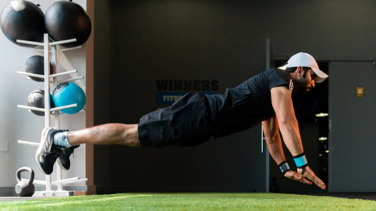 Middle Eastern man doing explosive pushups on gym turf.